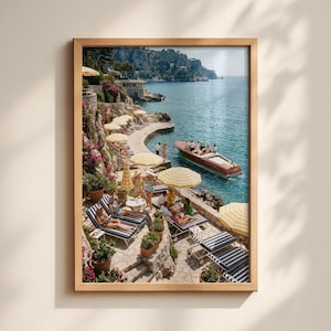 May include: A framed print depicting a coastal scene with a wooden boat, striped sun loungers, and yellow and white striped parasols. The image shows a sunny day with people relaxing by the water, surrounded by greenery and stone pathways.