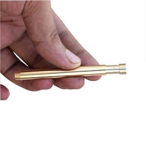May include: A gold-coloured, cylindrical metal object with a telescoping design. The object is held in a hand against a white background. The object appears to be a smoking pipe.