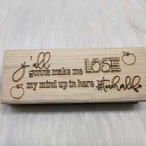 May include: Wooden sign with the text "Y'all gonna make me lose my mind up in here #teacherlife" with a red apple graphic on each side.