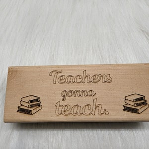 May include: A wooden sign with the text "Teachers gonna teach."  The sign has a stack of books on each side of the text.