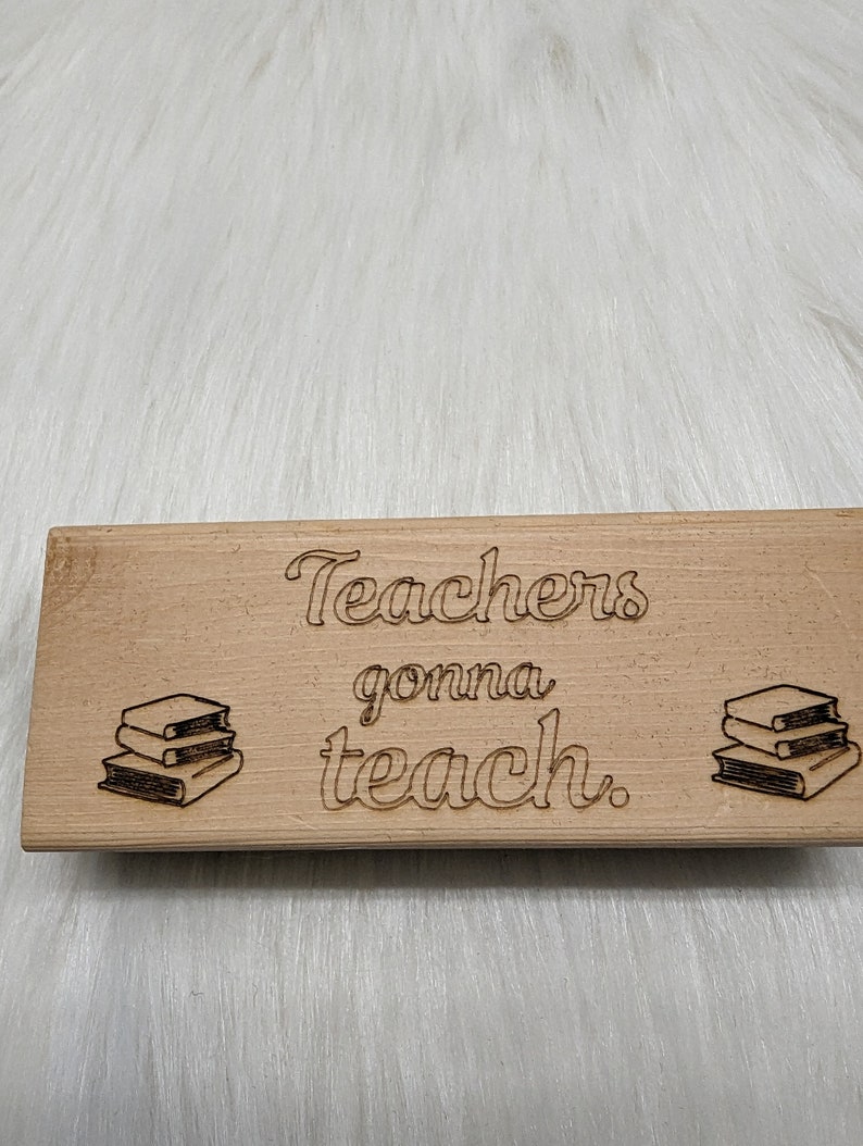 May include: A wooden sign with the text "Teachers gonna teach."  The sign has a stack of books on each side of the text.