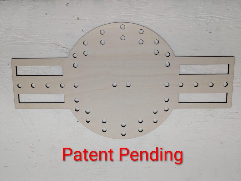 May include: A light-coloured wooden craft template featuring a central circular section with numerous small holes arranged in a ring, flanked by two rectangular side extensions with horizontal slots and additional holes. The text Patent Pending is below.