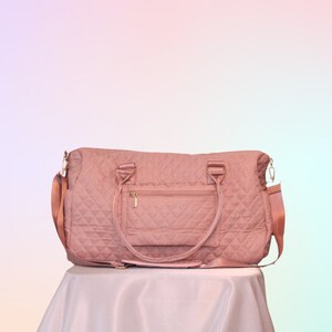 May include: A quilted pink travel bag with a gold zipper and a small pocket on the front. The bag has two top handles and a long adjustable strap.