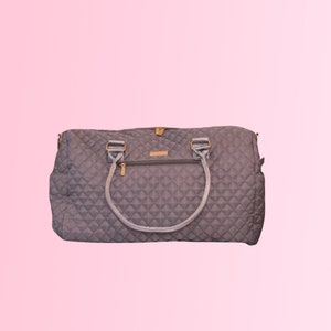 May include: A gray quilted travel bag with a gold zipper and two handles.