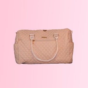 May include: A quilted cream-colored travel bag with white handles and gold accents.