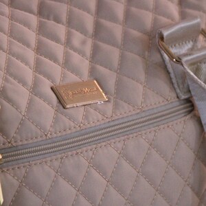 May include: A beige quilted travel bag with a gold zipper and a gold metal logo that says "Simply Vera Vera Wang".