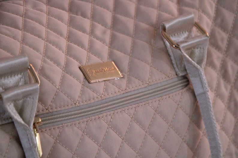 May include: A beige quilted travel bag with a gold zipper and a gold metal logo that says "Simply Vera Vera Wang".