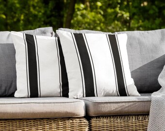 May include: A wicker patio sofa with two black and white striped pillows and a gray throw blanket with white fringe.