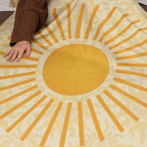 May include: A yellow and white throw blanket with a large sun design. The sun has a yellow center and yellow rays.