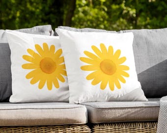 May include: Two white throw pillows with yellow daisy designs on a wicker patio couch with a gray throw blanket.
