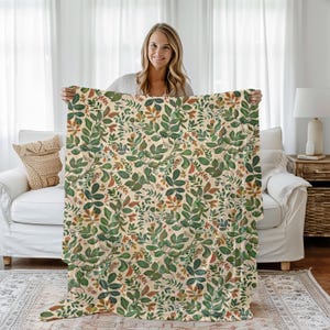 May include: A cream-colored throw blanket with a green and orange floral pattern. The blanket is made of a soft, comfortable fabric and features a repeating pattern of leaves and flowers.