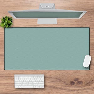 Op de afbeelding: Een lichtblauwe bureau mat met een herhalend patroon van overlappende cirkels. De mat ligt op een houten oppervlak met een computermonitor, toetsenbord en muis.