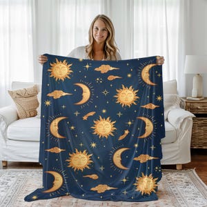 May include: A navy blue blanket featuring a celestial design with gold suns, crescent moons, stars, and clouds. The blanket is soft and cozy, perfect for adding a touch of whimsy to any room. The blanket is a standard size.