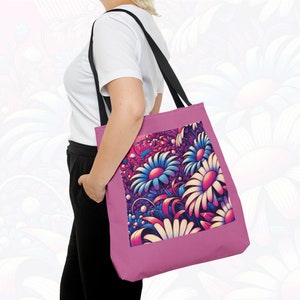 May include: A pink tote bag with black straps and a colorful floral print. The print features a variety of flowers in shades of blue, pink, and white.