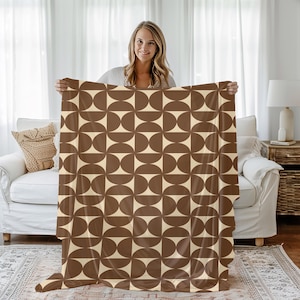 May include: A brown and cream throw blanket with a geometric pattern of overlapping circles. The blanket is being held up by a person.