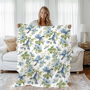 May include: White throw blanket with a repeating pattern of blue hummingbirds and blue flowers. The blanket is soft and cozy, perfect for snuggling up on the couch.
