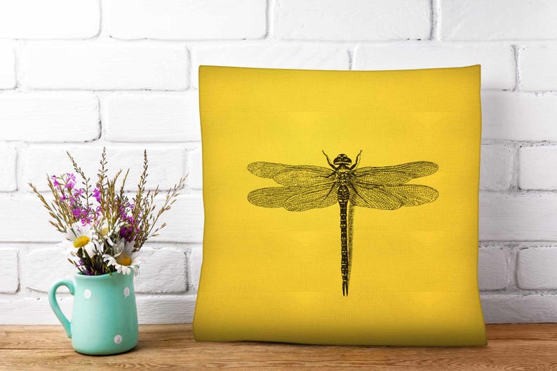 May include: A square throw pillow in a vibrant yellow color featuring a detailed black line art illustration of a dragonfly centered on the front. The dragonfly has intricate wing patterns and a segmented body, providing a high contrast design.