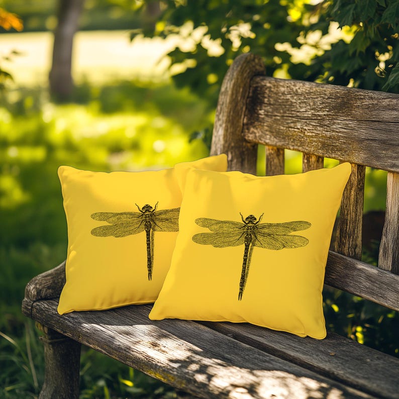 May include: Two square throw pillows in a bright yellow color, each featuring a detailed black line drawing of a dragonfly centered on the front. The pillows are positioned side by side, displaying the same insect illustration on both items.