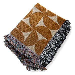 May include: A woven throw blanket with a geometric pattern of brown and white semi-circles. The blanket has a black and white fringe.