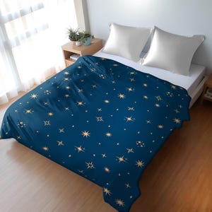 Puede incluir: Una funda nórdica azul con un patrón de estrellas doradas. La funda nórdica está en una cama con almohadas blancas.