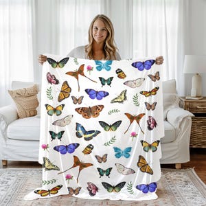 May include: White throw blanket with a colorful butterfly pattern. The blanket features a variety of butterfly species in shades of blue, yellow, orange, and green.