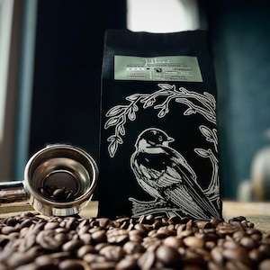 May include: A black bag of coffee beans with a white bird illustration and the text "Inkheart Snowbird Mountain Coffee Co." and "Roasted, Flavored, Dark Cocoa".