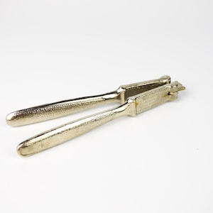Puede incluir: Un cascanueces de metal plateado con un acabado texturizado. El cascanueces está cerrado y listo para romper nueces.