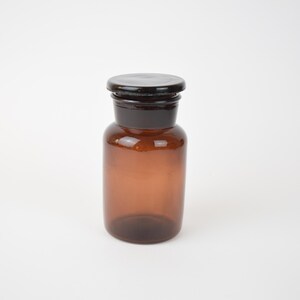 May include: A brown glass bottle with a black lid. The bottle is empty and has a round shape.
