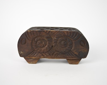 May include: A wooden pencil holder carved in the shape of a fish with two large eyes and a detailed design. The holder has 12 holes for pencils.