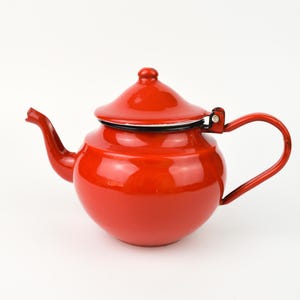 May include: A red enamel teapot with a rounded body, curved spout, and a matching lid. The handle is a simple loop, and the teapot has a black rim. This kitchenware item is a classic design.
