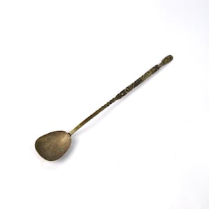Op de afbeelding: Een lange, sierlijke, zilverkleurige lepel met een ronde kom. De lepel heeft een decoratief ontwerp op de steel.