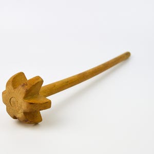 Puede incluir: Una paleta de mantequilla de madera con una cabeza en forma de estrella y un mango largo y redondeado. La paleta está hecha de madera de color claro y está colocada sobre un fondo blanco. Este utensilio de cocina se utiliza para hacer mantequilla.