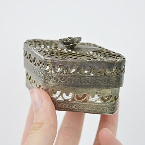 May include: A silver metal trinket box with a delicate floral design and a rose-shaped knob on the lid.
