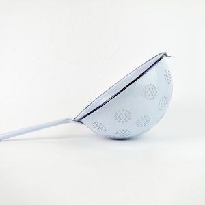 May include: A white enamel colander with a blue rim and a handle. The colander has a pattern of small circles.