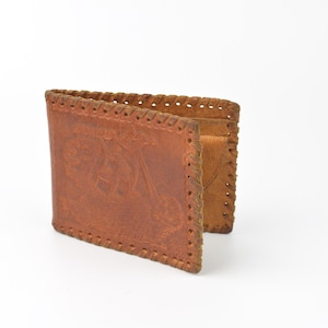 May include: A brown leather wallet with an embossed design. The wallet is open, showing the interior compartments. The edges are stitched with a decorative pattern. The wallet is made of light brown leather.