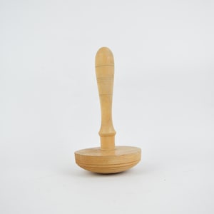 Könnte beinhalten: Ein Werkzeug aus Holz mit einer runden Basis und einem langen Griff. Das Werkzeug ist aus hellbraunem Holz gefertigt und hat eine glatte Oberfläche.