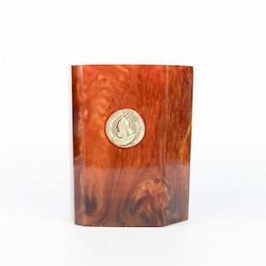 Op de afbeelding: Een rechthoekige, bruin en oranje gemarmerde container met een goudkleurig embleem. De container heeft een glanzende afwerking en een unieke, getextureerde uitstraling. Het embleem is cirkelvormig en toont een profiel.