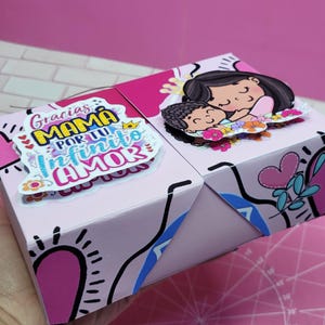 May include: A pink and blue gift box with a colorful design and the text "Gracias Mam&aacute; por tu infinito amor". The box features a cartoon illustration of a mother and child.