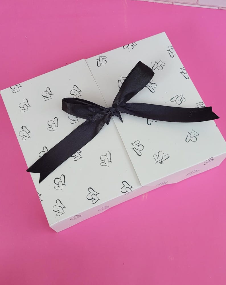 May include: A white gift box with a black ribbon tied in a bow. The box is decorated with a repeating pattern of small hearts.