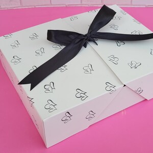 May include: A white gift box with a black ribbon tied in a bow. The box is decorated with a repeating pattern of small hearts.