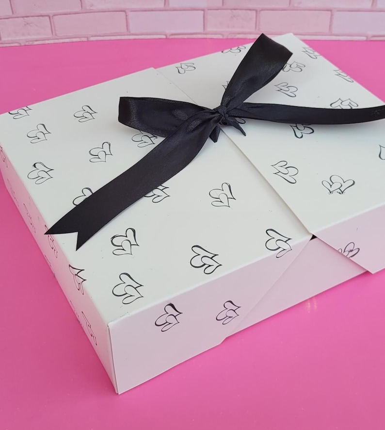 May include: A white gift box with a black ribbon tied in a bow. The box is decorated with a repeating pattern of small hearts.