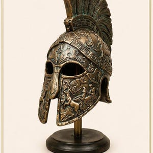 Könnte beinhalten: Bronze-farbener dekorativer Helm mit aufwendigen Reliefdetails, einschließlich Kamm und Gesichtsschutz. Der Helm ist auf einem schwarzen Holzsockel mit einem goldfarbenen Ständer montiert. Das Wort "MİĞFER" ist unten aufgedruckt.