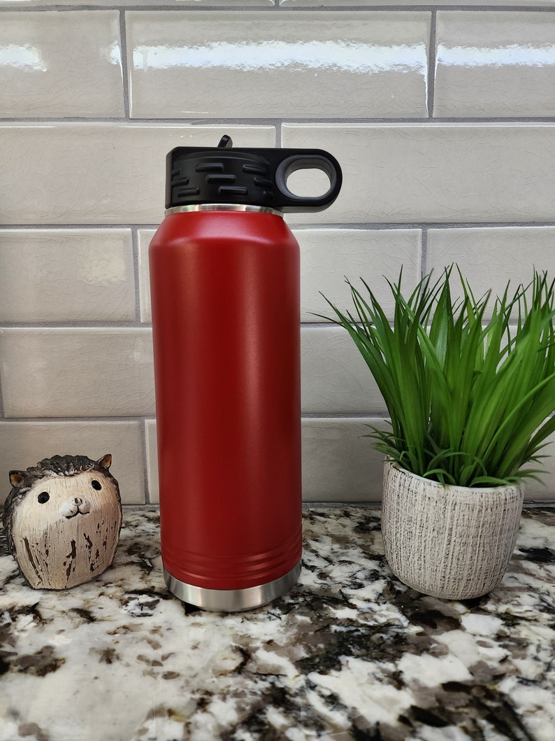 K&ouml;nnte beinhalten: Eine rote Edelstahl-Wasserflasche mit schwarzem Deckel und Griff. Die Flasche steht auf einer Granit-Arbeitsplatte.