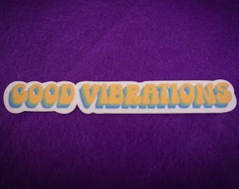 May include: A white sticker with the text "GOOD VIBRATIONS" in yellow and blue letters with a 3D effect. The sticker is on a purple background.