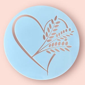 May include: A light blue plastic stencil with a heart shape and a wheat stalk design. The stencil is perfect for decorating cakes, cookies, and other baked goods.