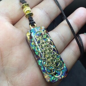 May include: A gold-toned flower of life pendant with a black cord necklace. The pendant is made of resin and has a iridescent finish.