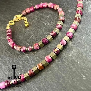 Può includere: Un set di due collane, una con perline rosa e dorate e l'altra con perline dorate e rosa. Le collane sono su una superficie grigio scuro.  "Offerta speciale" è scritto su un nastro dorato.