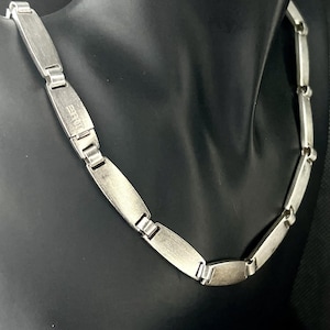 Può includere: Una collana a catena d'argento con finitura spazzolata e un'etichetta rettangolare con la scritta "BRUT".