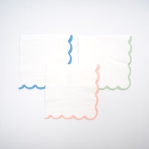 May include: Three white paper napkins with scalloped edges. The napkins have a blue, green, and pink trim.