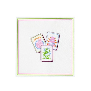 May include: Square white paper napkin with a green and pink border. The napkin features three playing cards with colorful illustrations: a joker card, a pagoda card, and a dragon card.